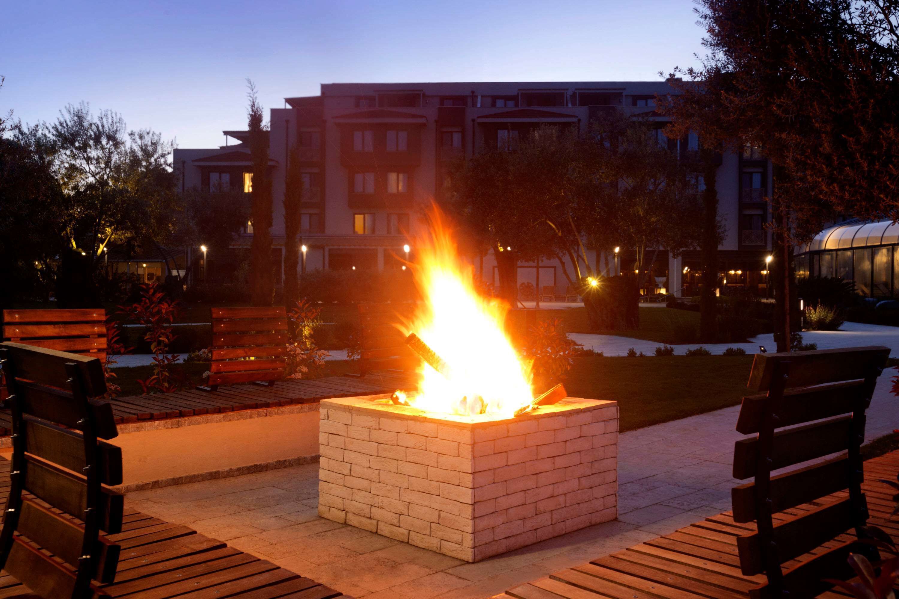 A square fire pit with a fire burning in the center, surrounded by benches.