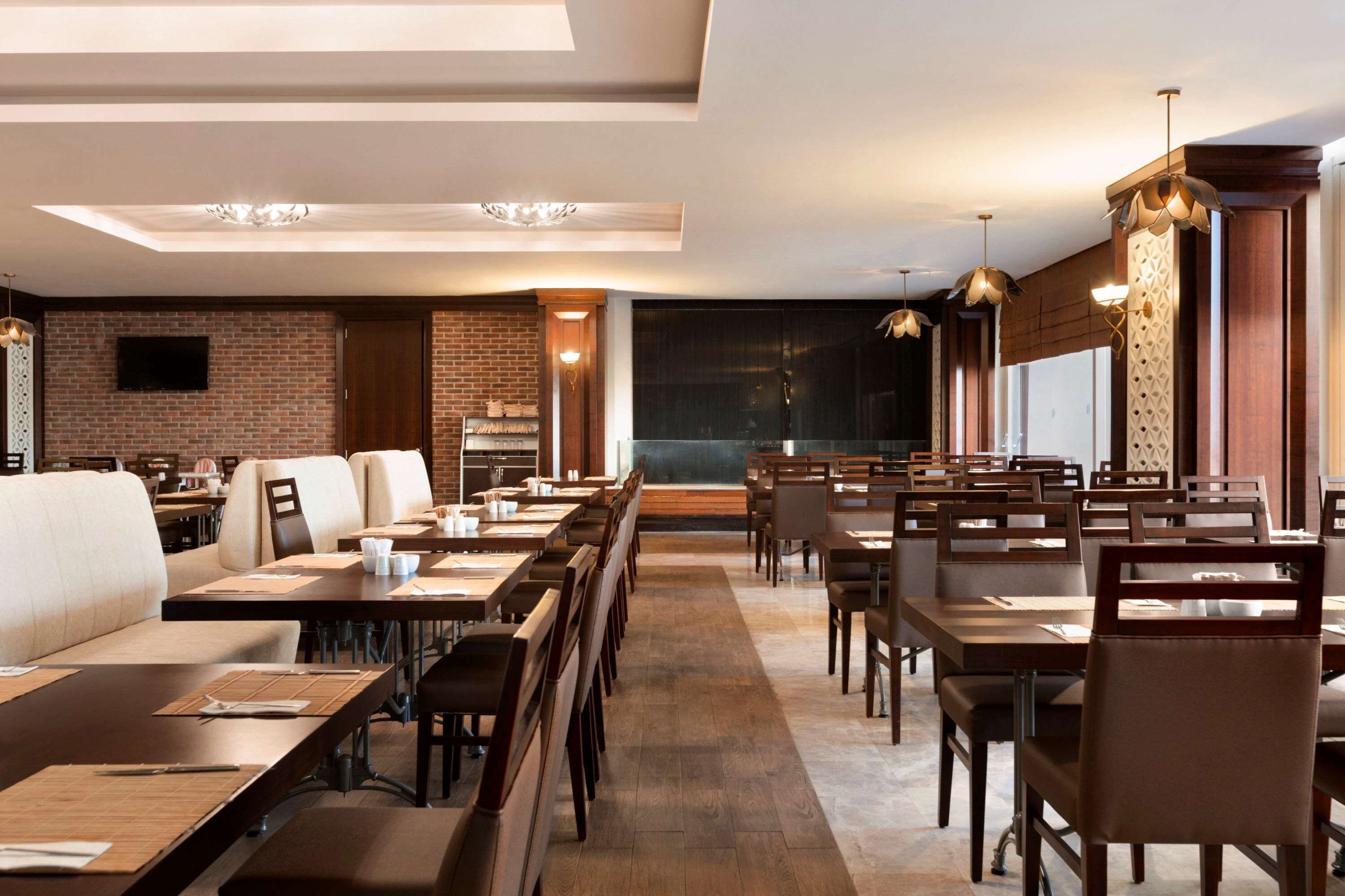 Un restaurante moderno con mesas y sillas de madera, pared de ladrillo e iluminación colgante.
