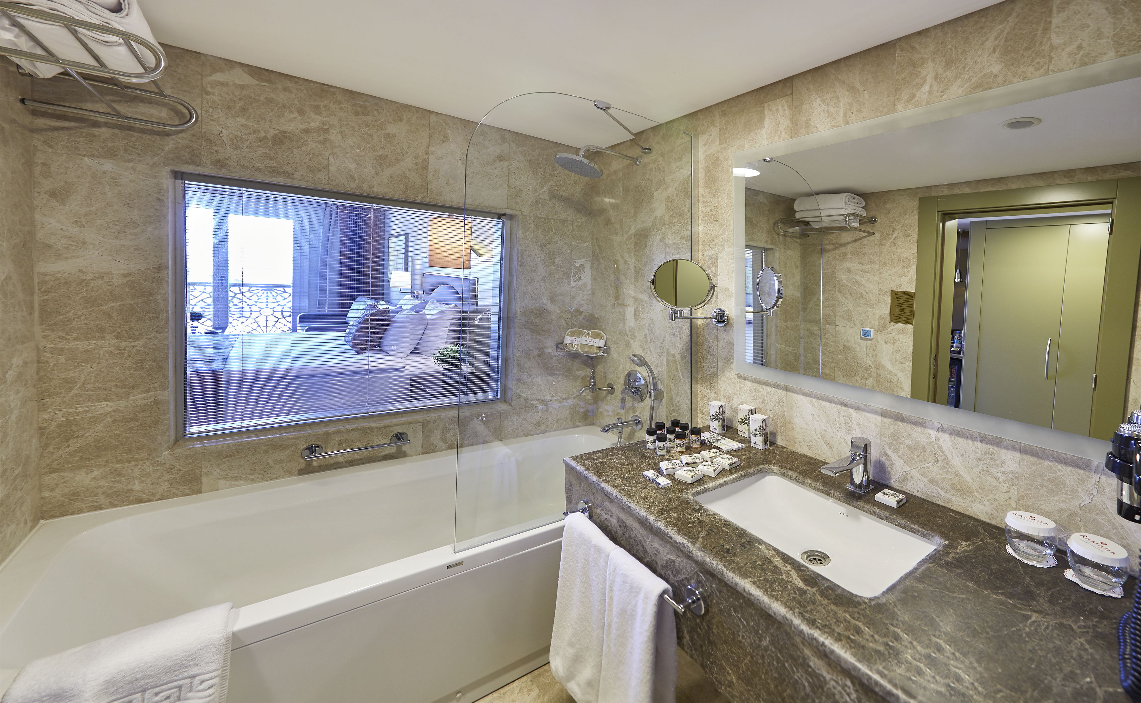 A modern bathroom with a bathtub, two sinks, a large mirror, and a window with blinds.
