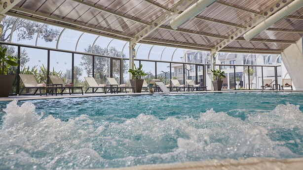 An indoor swimming pool with lounge chairs and potted plants.