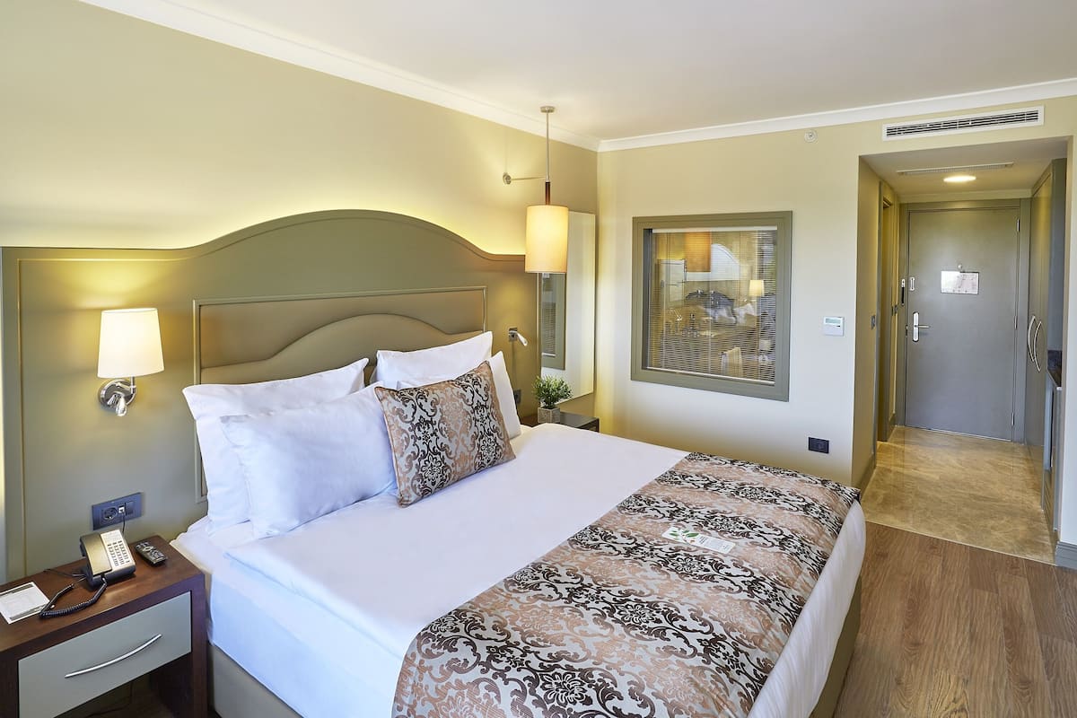 A hotel room with a large bed, bedside lamps, a telephone, and a door leading to a bathroom.
