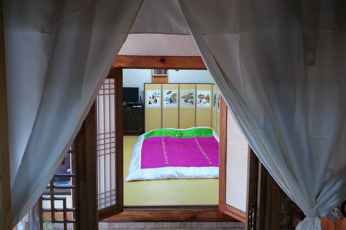 A room with a bed, a wooden cabinet, and a window with a view of the outside.