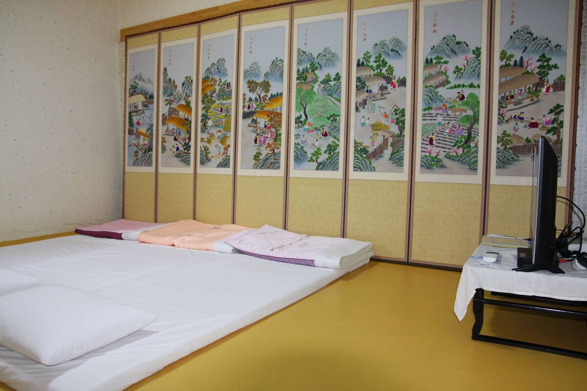 A room with a bed, a desk with a computer, and a traditional Japanese sliding door with artwork.