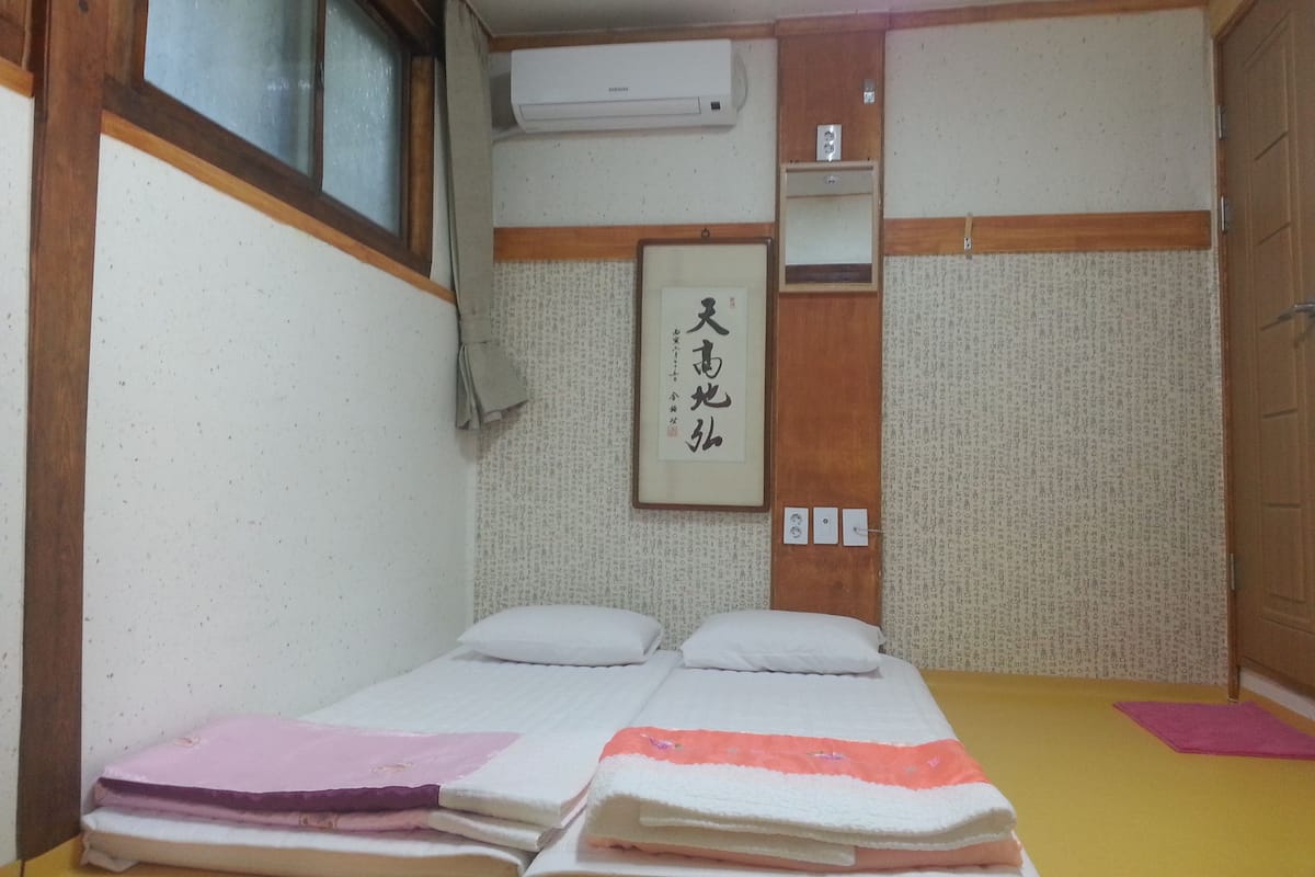 A traditional Japanese-style room with tatami flooring, a bed with white bedding, a wooden wardrobe, and a wall-mounted air conditioner.