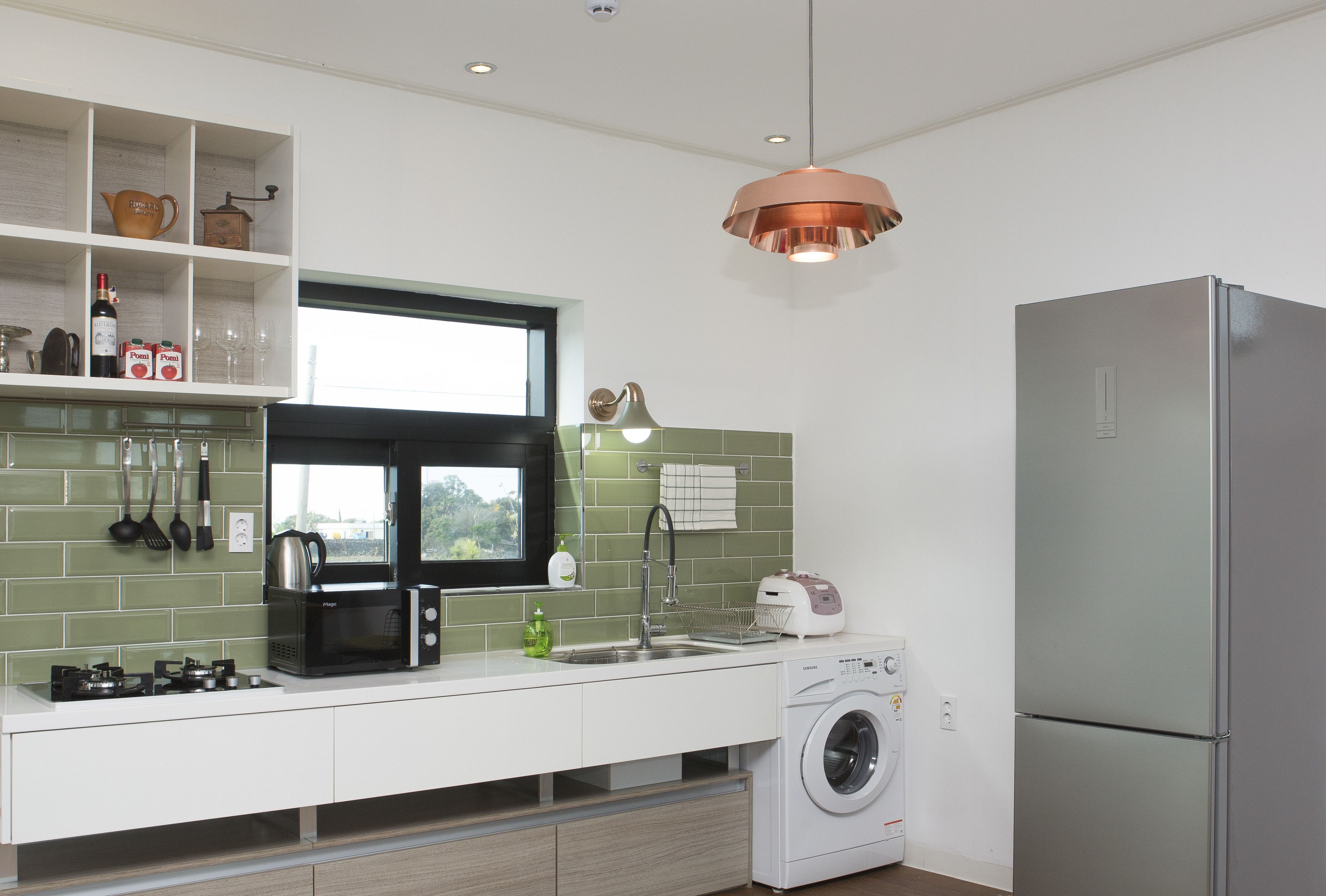 Een moderne keuken met een ingebouwde wasmachine, een roestvrijstalen koelkast en een raam met uitzicht op groen.