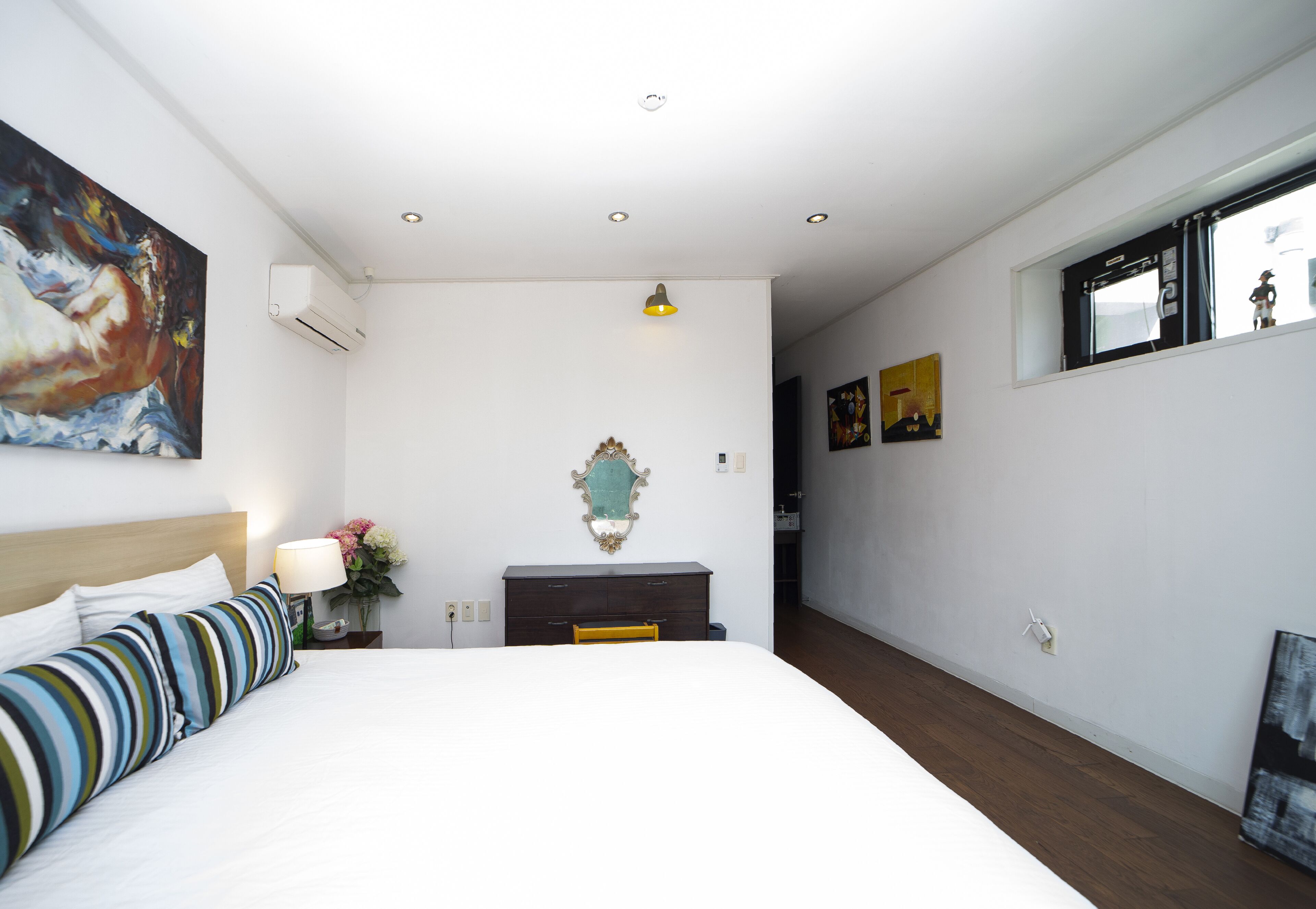 A bedroom with a bed, a dresser, a mirror, and a painting on the wall.