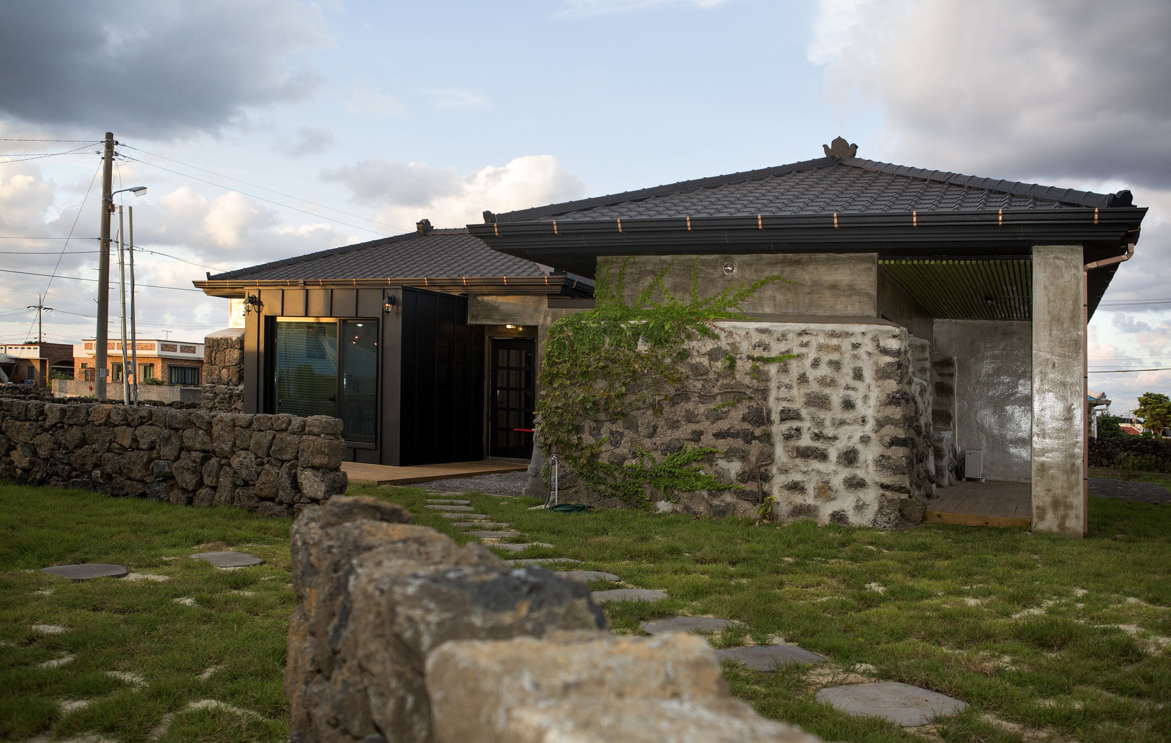 Een modern huis met een stenen gevel, een houten terras en een gazon met staptegels.