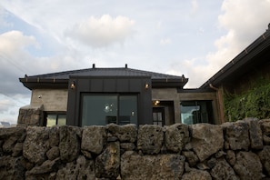 A modern house with a stone wall in front, large windows, and a sloped roof. - Casa Bonbon (Jeju City)
