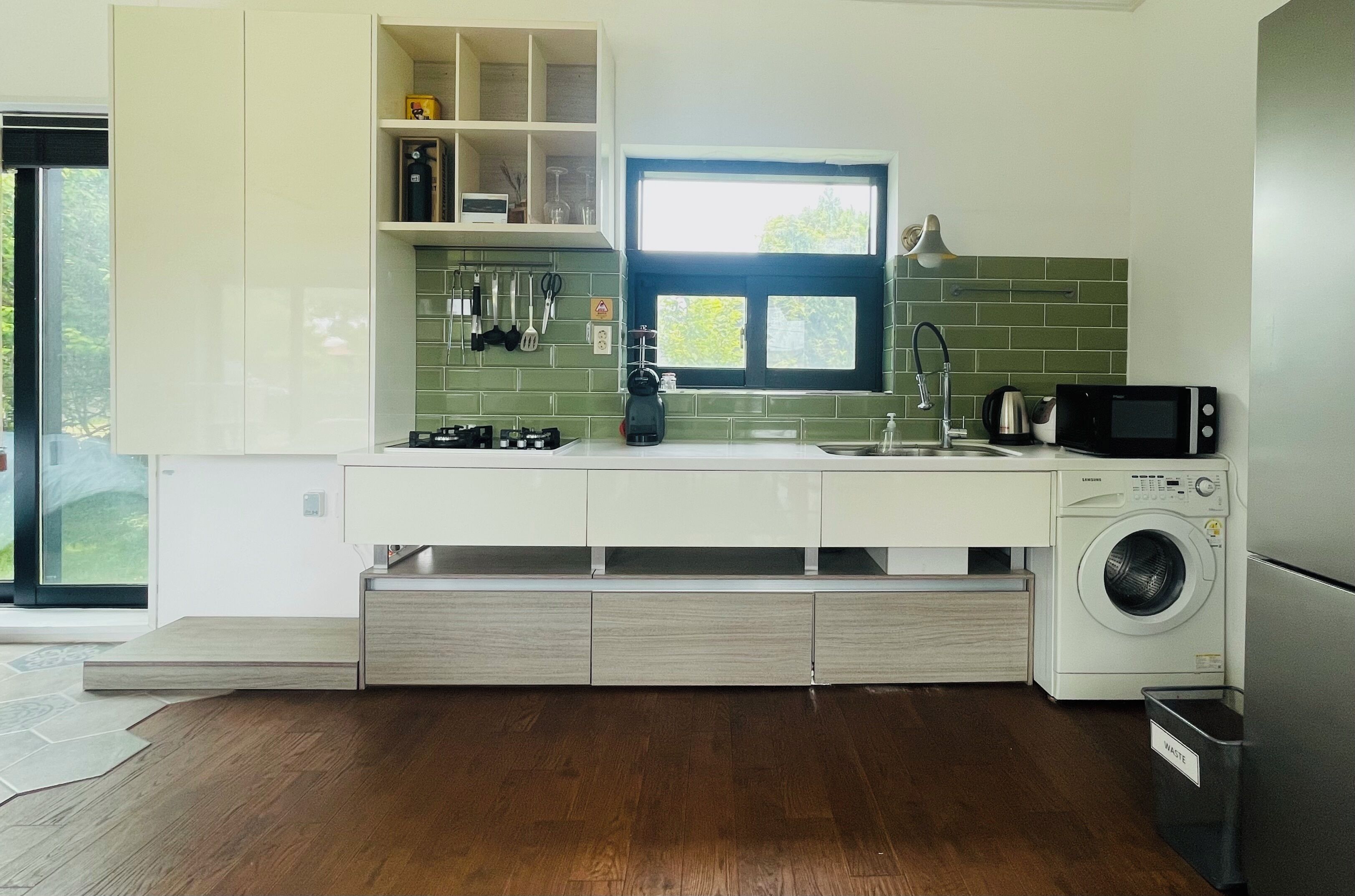 A modern kitchen with a built-in washing machine, a window with a view, and a countertop with various appliances.