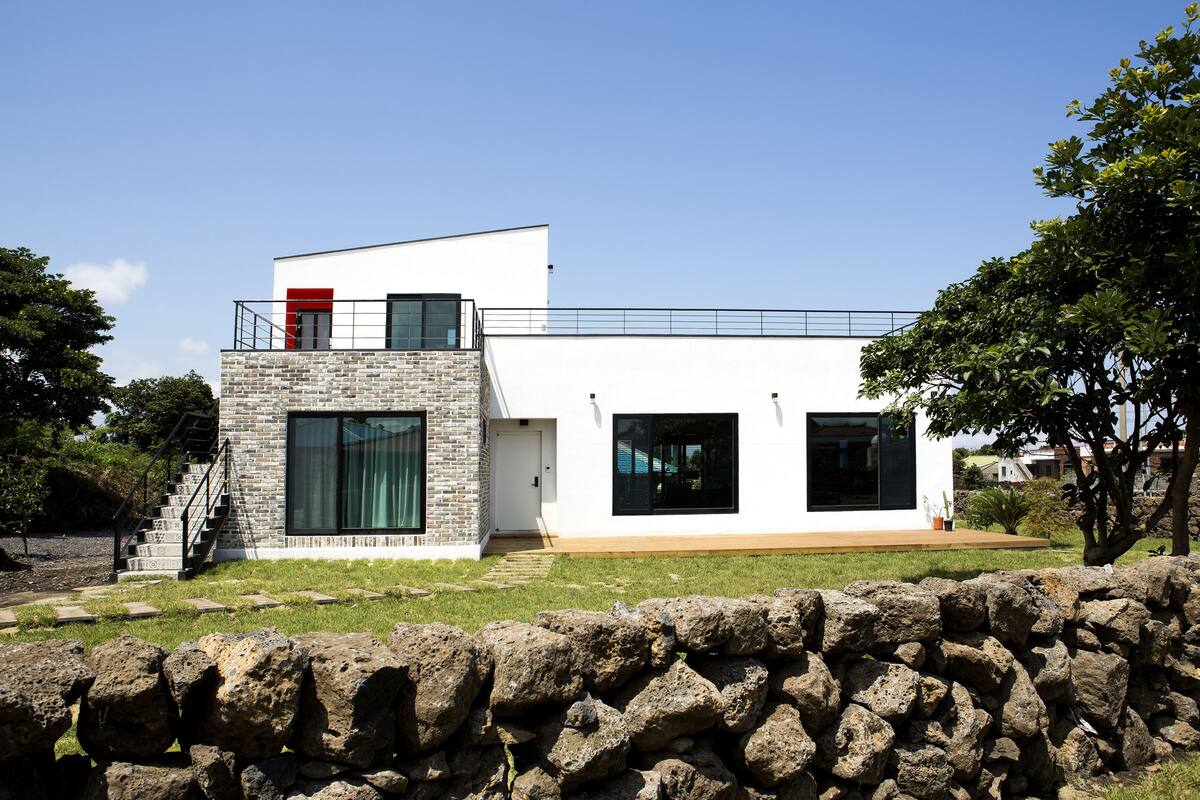 A modern two-story house with a stone facade, large windows, and a red door.