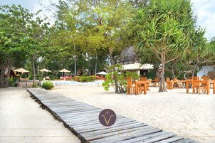 A beachside resort with wooden deck seating, palm trees, and a sandy beach.