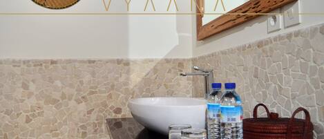 Une salle de bain avec un mur recouvert d’une mosaïque de pierre, un lavabo blanc et un miroir doté d’un cadre en bois.