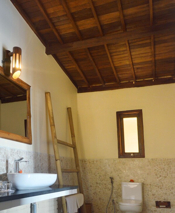 A bathroom with a wooden ceiling, a white sink, a mirror, and a shower.