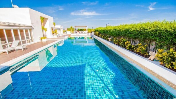 A swimming pool with clear blue tiles, surrounded by white buildings and greenery. - Hyde Park Residence by PSR ASIA (Pattaya)