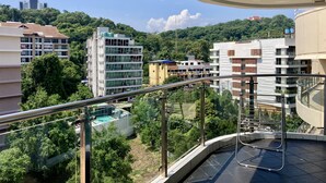 A balcony with a glass railing overlooking a residential area with various buildings and greenery. - Hyde Park Residence by PSR ASIA (Pattaya)