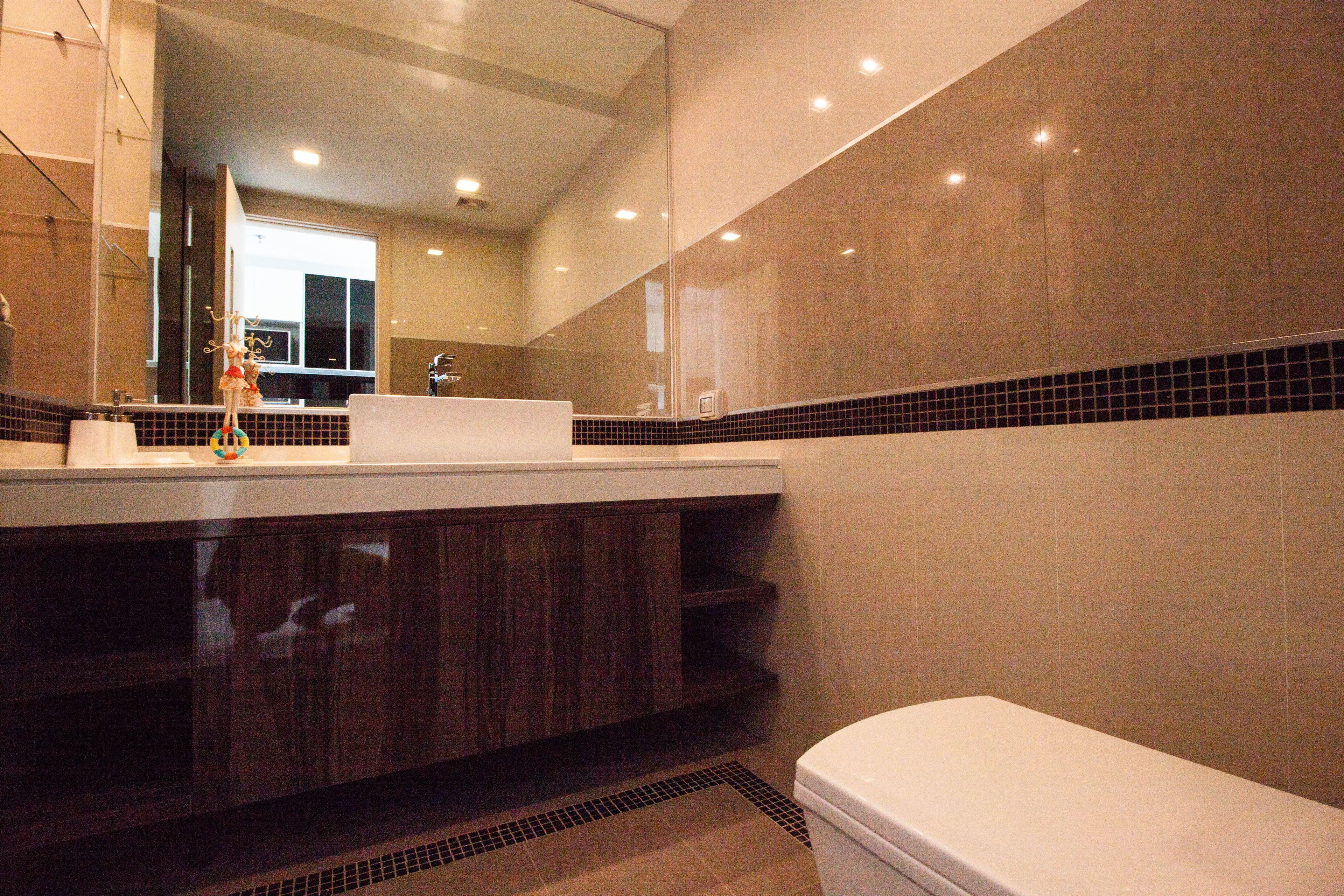 A modern bathroom with a large mirror, dark wood cabinetry, a white toilet, and a tiled backsplash.