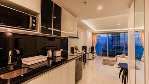 A modern kitchen with a built-in microwave, a coffee machine, and a sink. There is a dining area with a table and chairs, and a large window offering a view of the city. - Wongamat Tower by Pattaya Sunny Rentals (Pattaya)