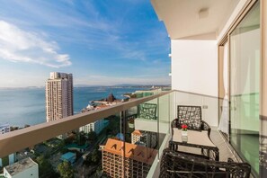 Enjoy panoramic views of the city and water from this high-rise's spacious balcony, featuring a table and chair for relaxation or dining.