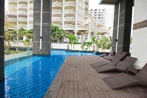 Relax by the pool surrounded by a wooden deck and lounge chairs, with a view of the surrounding area from the building's balconies.
