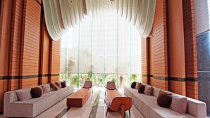 A modern hotel lobby with two sofas, a wooden coffee table, and a large window providing a view of greenery. - Wongamat Tower by Pattaya Sunny Rentals (Pattaya)