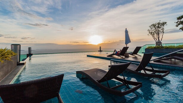 A poolside area with lounge chairs and a view of the sunset over the water. - Wongamat Tower by Pattaya Sunny Rentals (Pattaya)