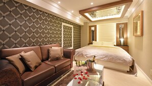 A modern hotel room with a large bed, a leather sofa, a glass coffee table with rose petals, and a champagne bottle. - Hotel Gransky - Adults Only (Tokyo)