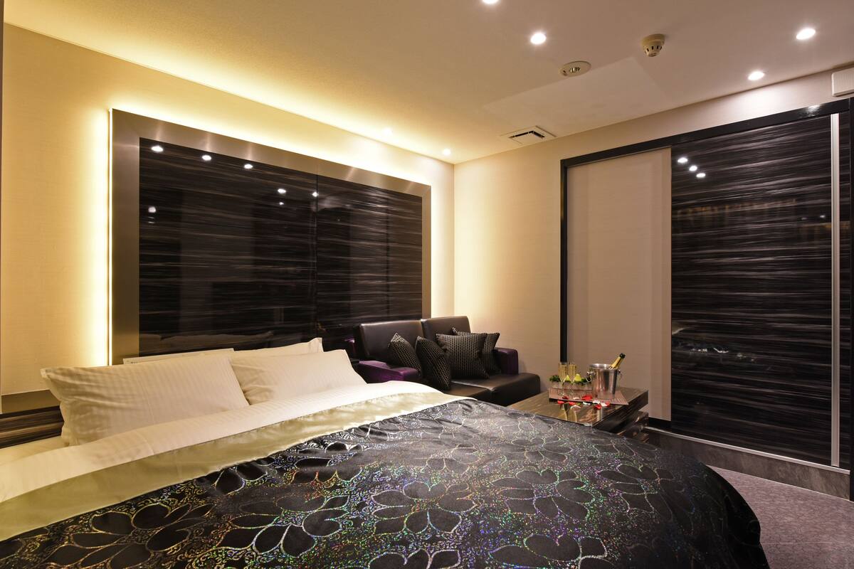 A modern bedroom with a large bed, a seating area with a sofa, and a large window.