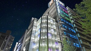 A modern hotel with a glass facade and illuminated signage, surrounded by other buildings. - Hotel Gransky - Adults Only (Tokyo)