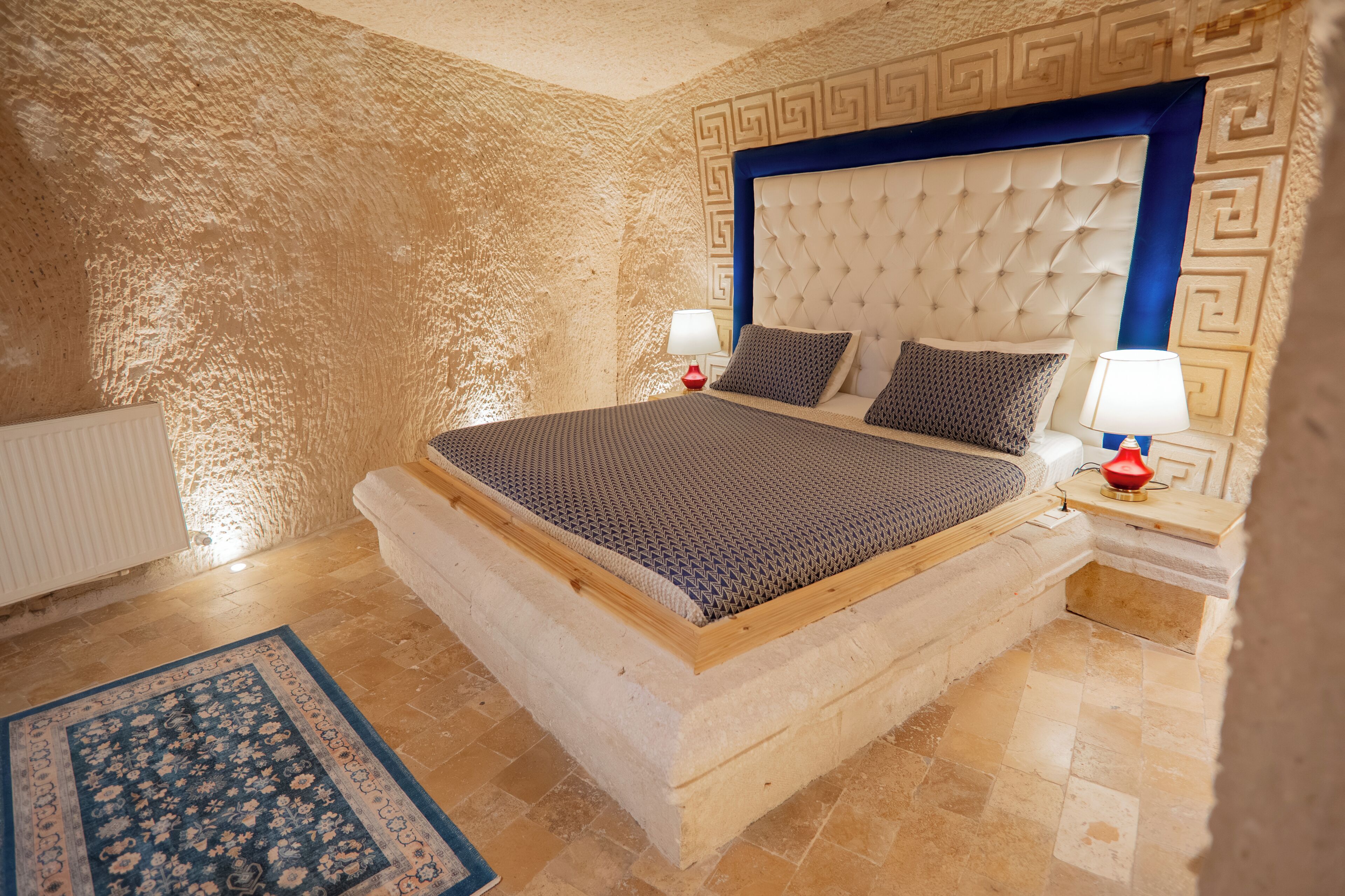 Une chambre à coucher avec un grand lit, une tête de lit ornée d’un motif géométrique, deux tables de chevet avec des lampes et un tapis à motifs.