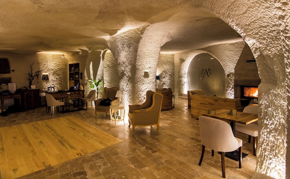 A spacious interior with high ceilings and natural stone walls, featuring a fireplace, seating areas, and a wooden floor.