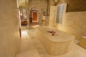 Ein Badezimmer mit einer Marmortonne, einer Dusche mit gemusterten Fliesen und einer Steinwand.