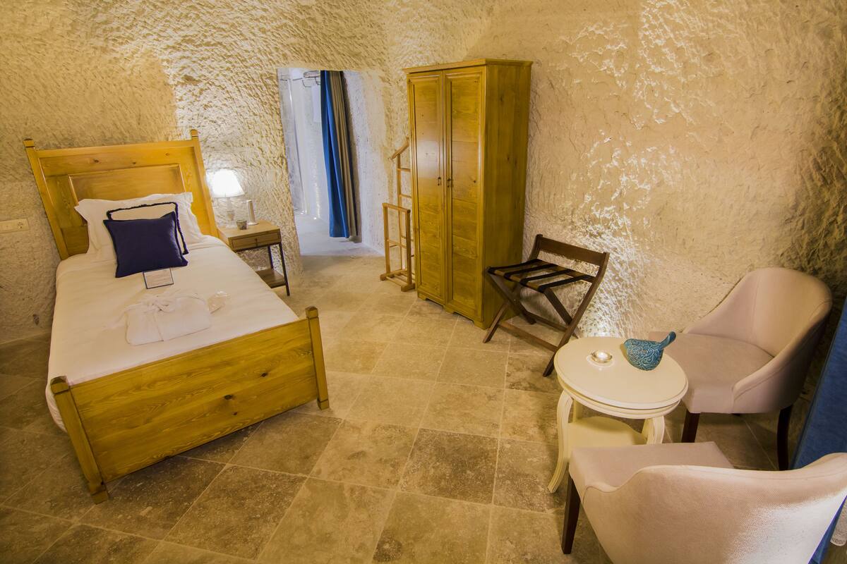 A bedroom with a wooden bed, a wardrobe, a chair, a small table, and a window with curtains.