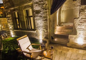A stone-walled room with a bathtub, a wooden chair, and a table with a candle and glasses.