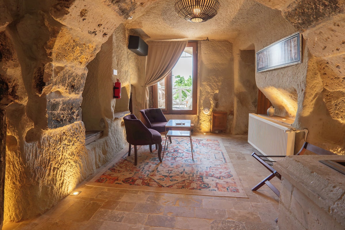 A room with a stone wall, a wooden table, a chair, and a window with curtains.