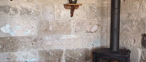 A rustic room with a stone wall, a wooden bench, a round mirror, and a black wood-burning stove.