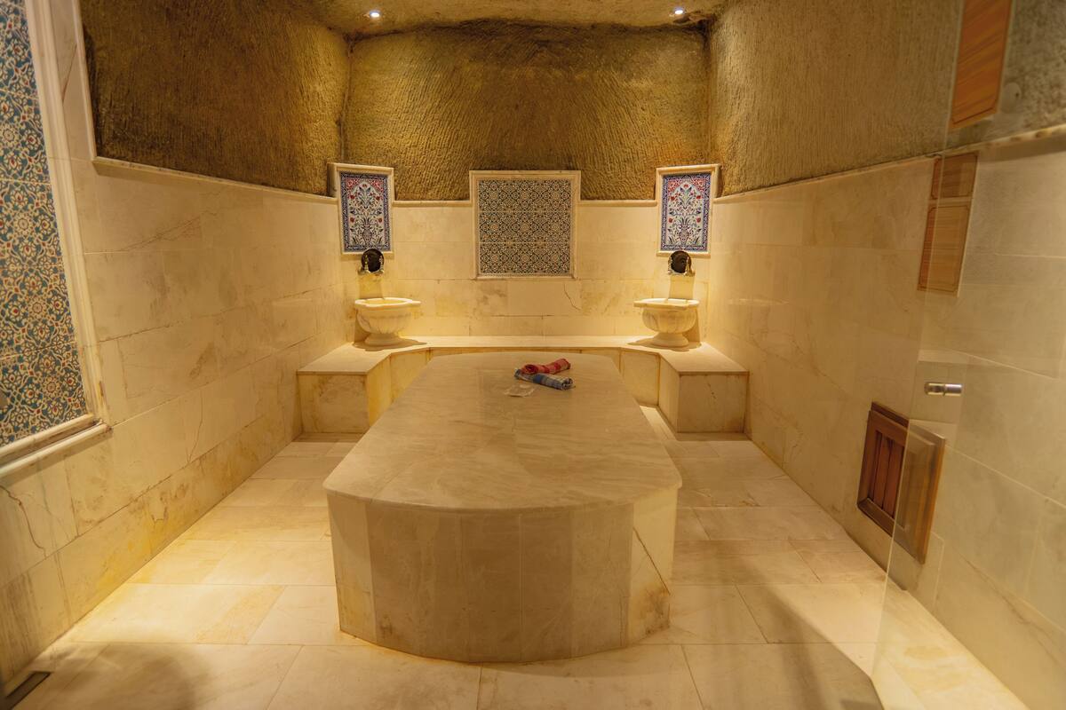 A bathroom with a central marble sink, two wall-mounted toilets, and decorative tiles.