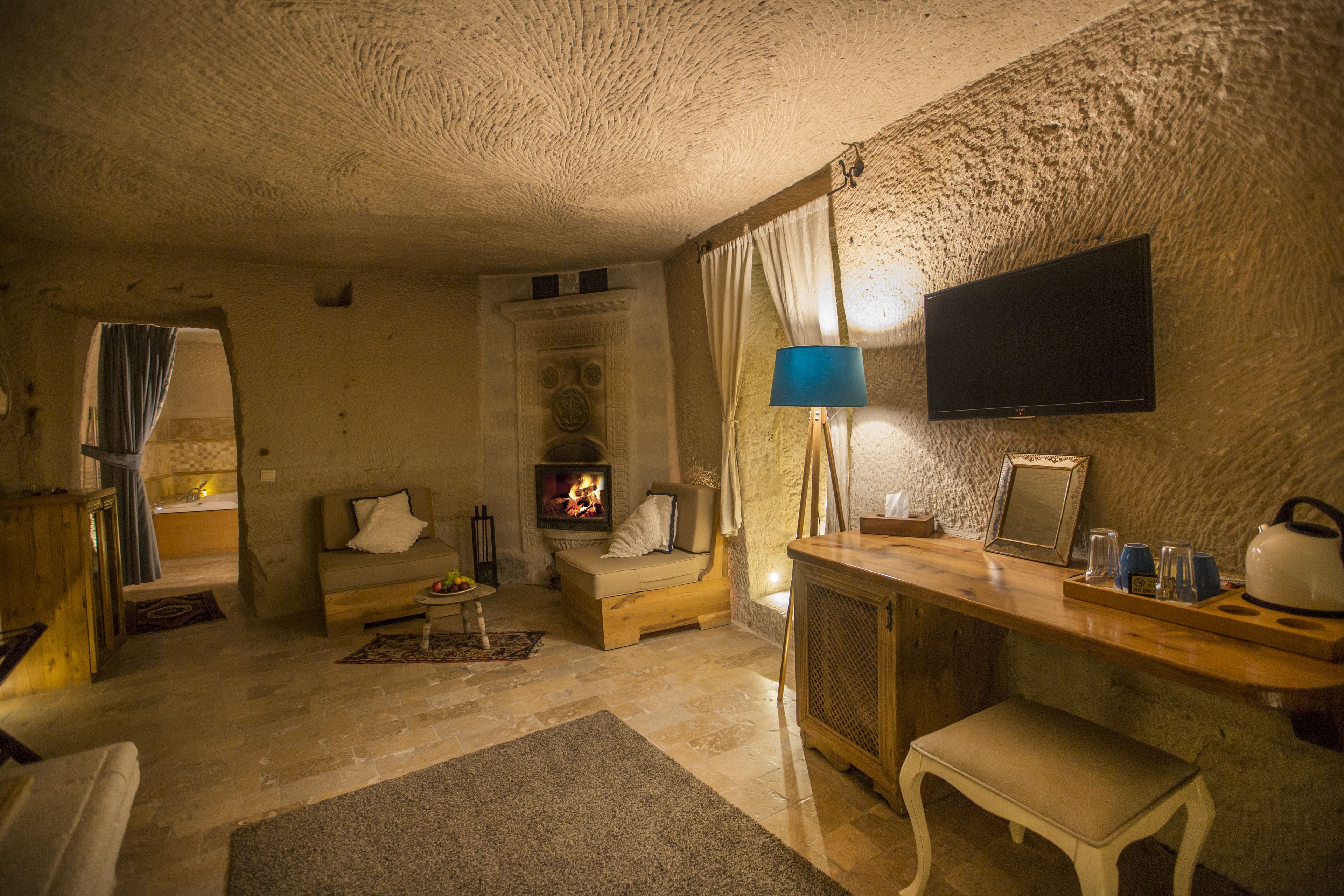 A cozy living room with a fireplace, a sofa, a wooden table, and a television mounted on the wall.