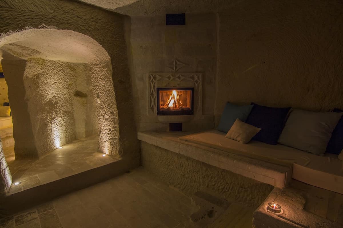 A stone-walled room with a fireplace, a stone bench, and a cushioned seating area.