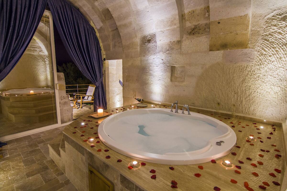 A stone-walled bathroom with a large bathtub, rose petals, and candles.