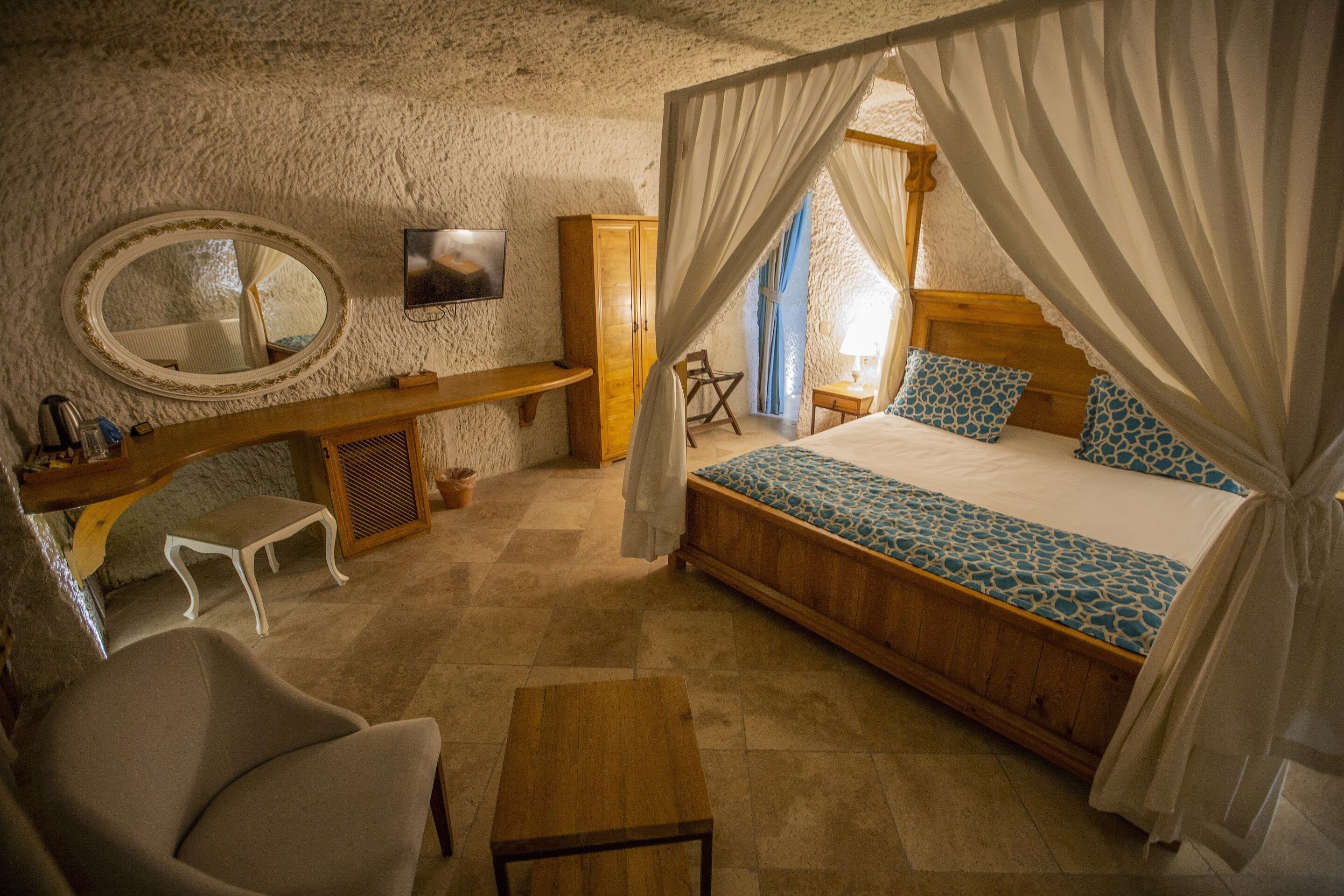 A bedroom with a bed, a bedside table, a chair, a desk, a mirror, a wardrobe, and a television.