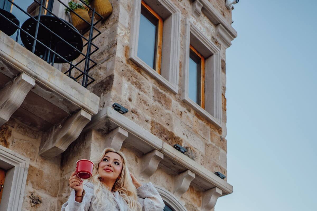 A woman standing on a stone balcony of a historic building, holding a red cup.