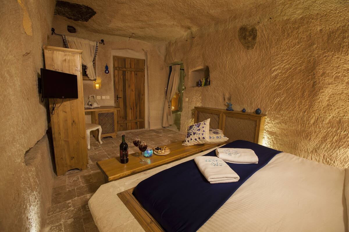 A rustic room with a bed, wooden furniture, a television, and a small table with wine glasses and a bottle.