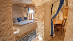 A bedroom with a stone wall, a bed, a wooden desk, and a chair. - Azure Cave Suites (Avanos)