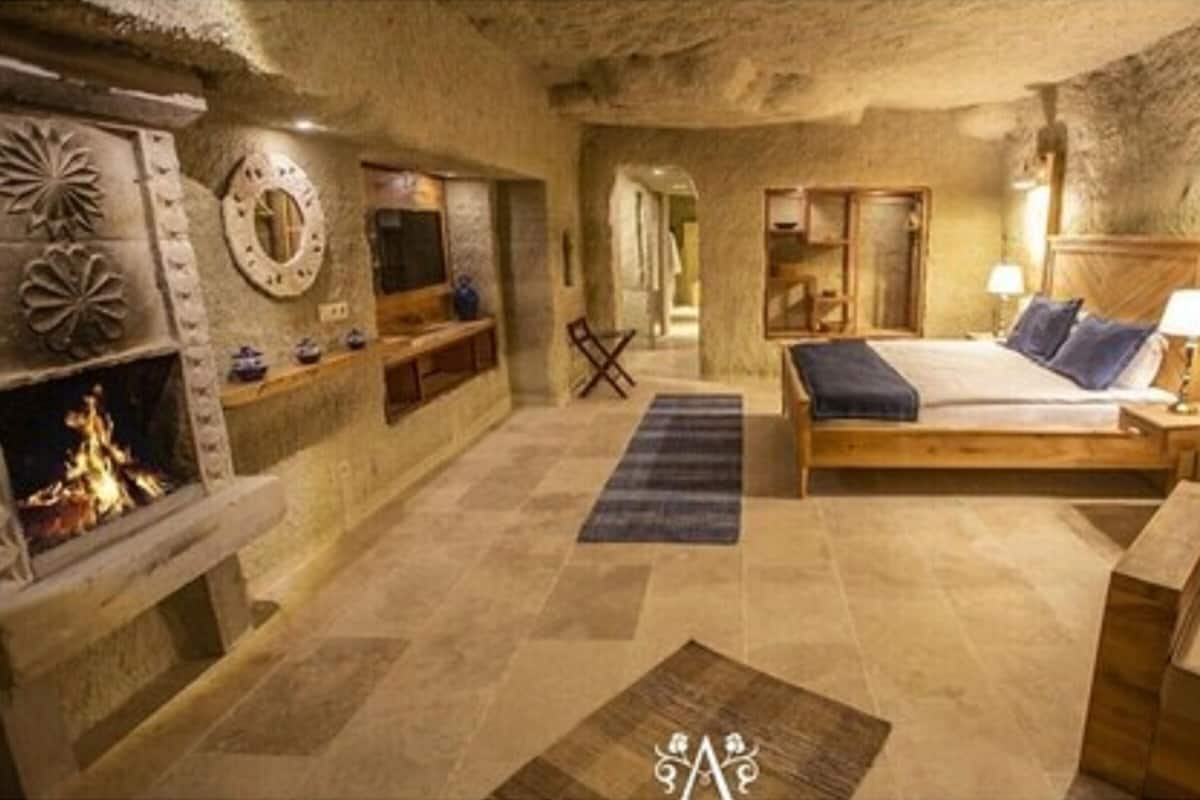 A rustic room with a stone fireplace, a bed with a wooden headboard, and a nightstand with a lamp.
