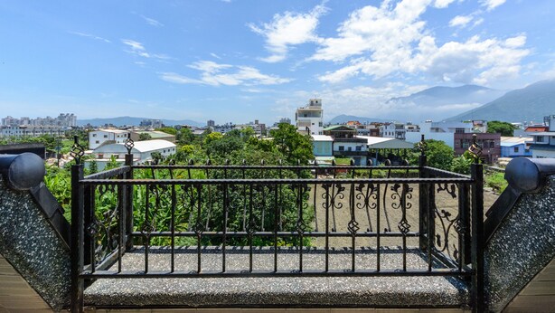 Un balcón con barandilla de metal que da a una vista urbana con edificios y montañas al fondo.