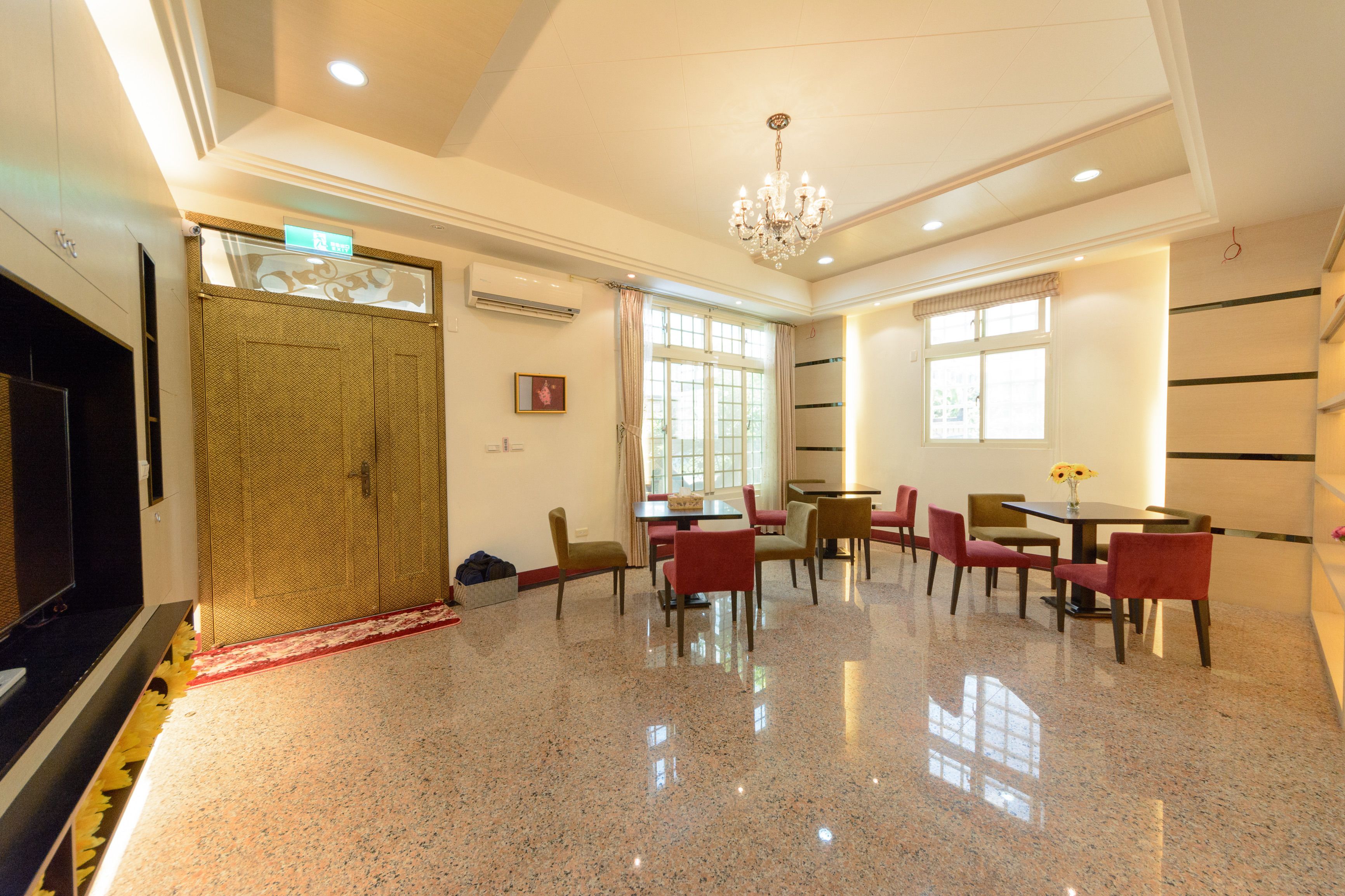 A spacious hotel lobby with a polished floor, a chandelier, and a seating area with tables and chairs.