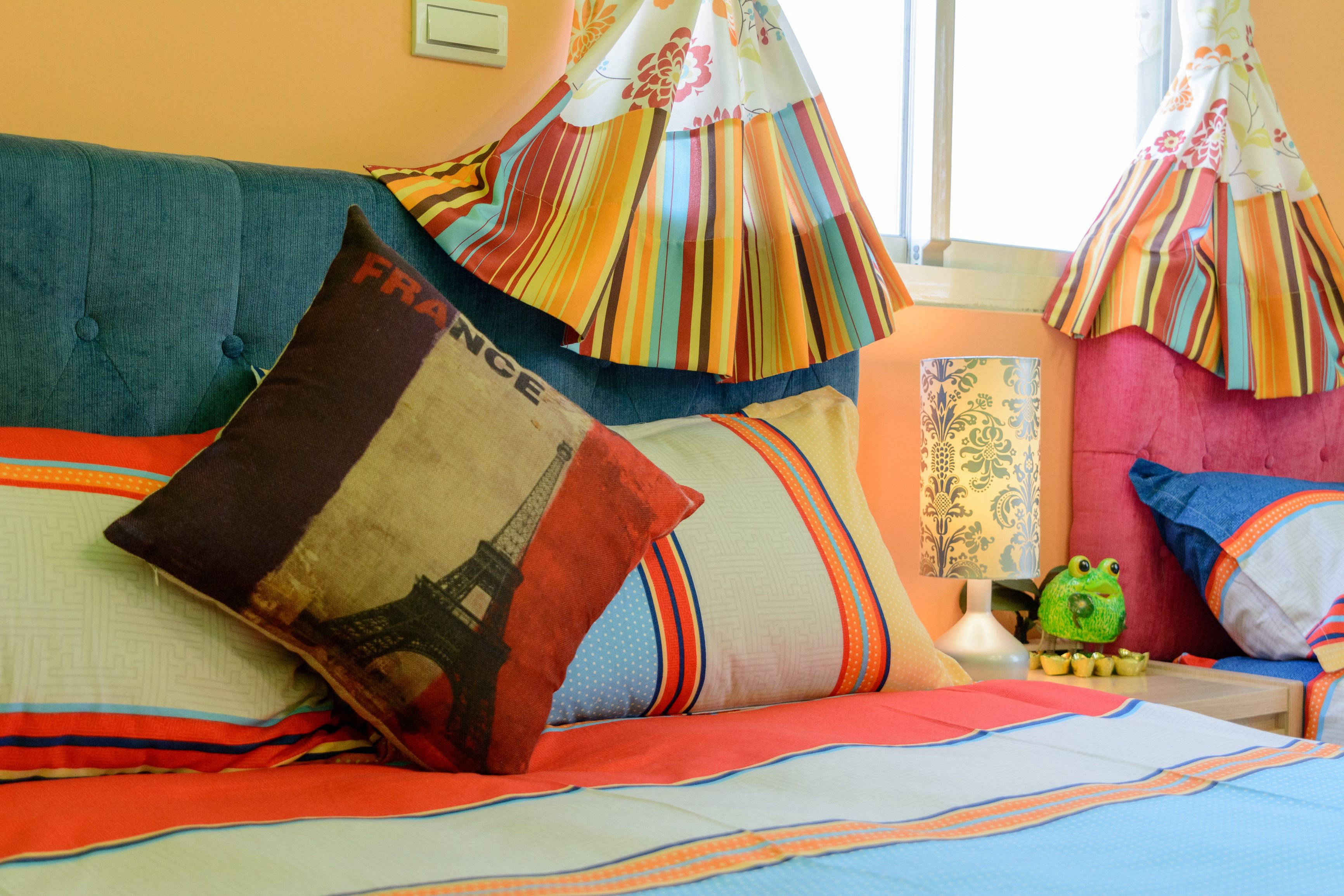 A bed with colorful pillows, a lamp, and a decorative frog figurine.