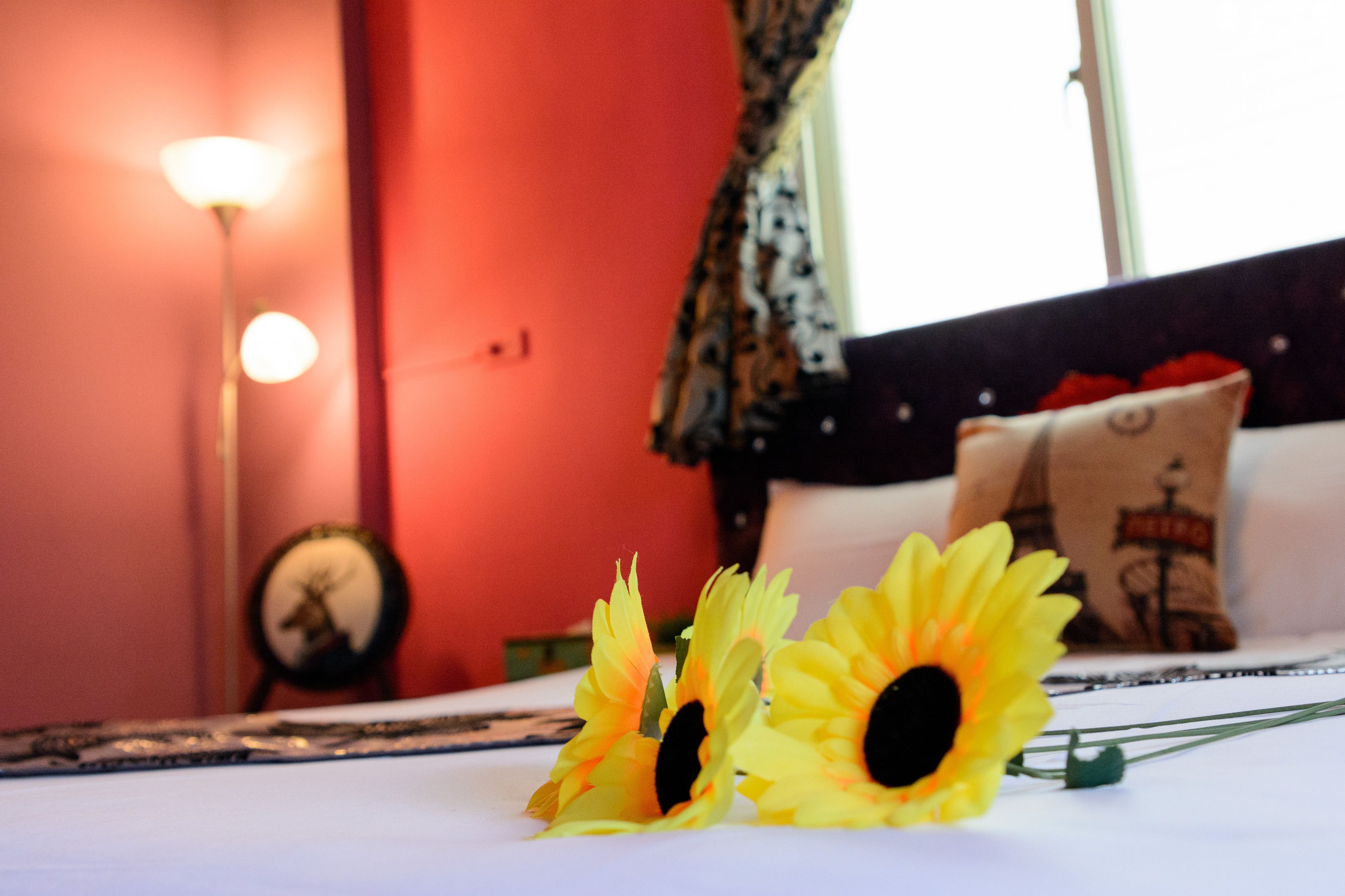 A bed with a white sheet, a pillow with a design, and two yellow flowers on the bed.