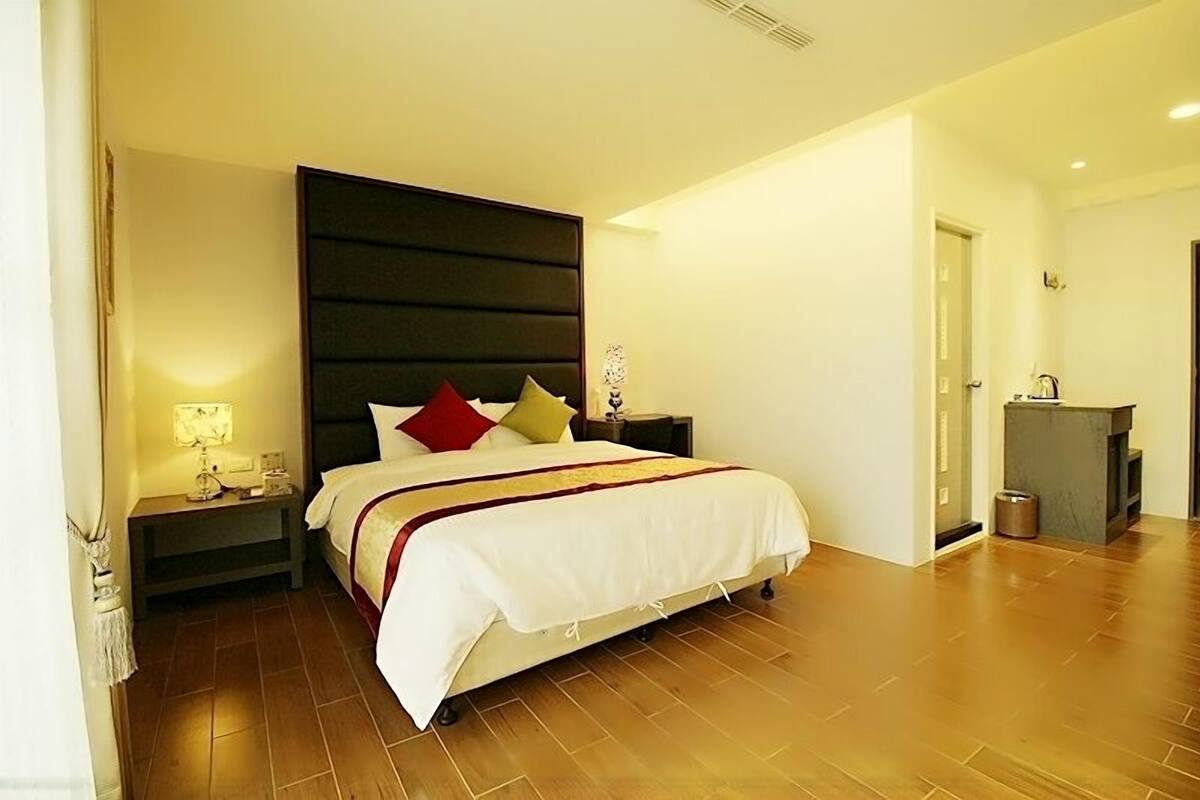 Habitación de hotel con una cama grande, una mesita de noche con lámpara y un pequeño escritorio con silla.