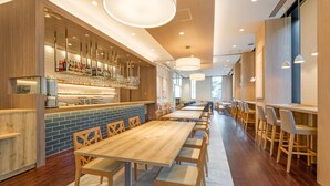 A modern restaurant with long wooden tables and chairs, a bar area with bottles and glasses, and pendant lighting. - Hotel Mystays Premier Akasaka (Tokyo)
